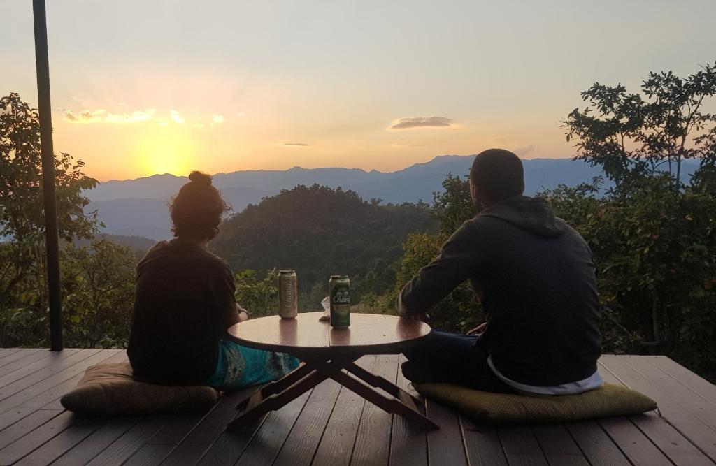 Zwei Leute sitzen am Tisch und beobachten den Sonnenuntergang. in der Unterkunft Monsonkeang Camping view ม่อนสันเกี๋ยง in Mae Chaem