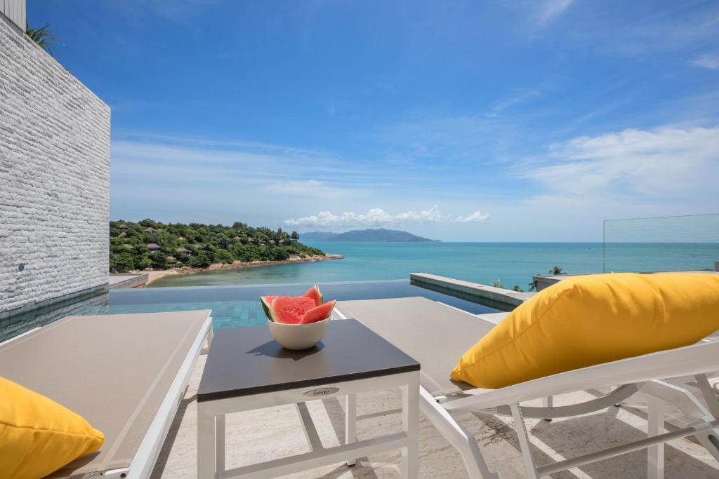 a table with a bowl of watermelon on a balcony with the ocean at BEACHSIDE VILLA - B18 - at Bayside Luxury Villas Samrong Bay Beach, 4 BED 5 BATH, SEA & SUNSET VIEWS, only 200m walk to the Beach in Choeng Mon Beach