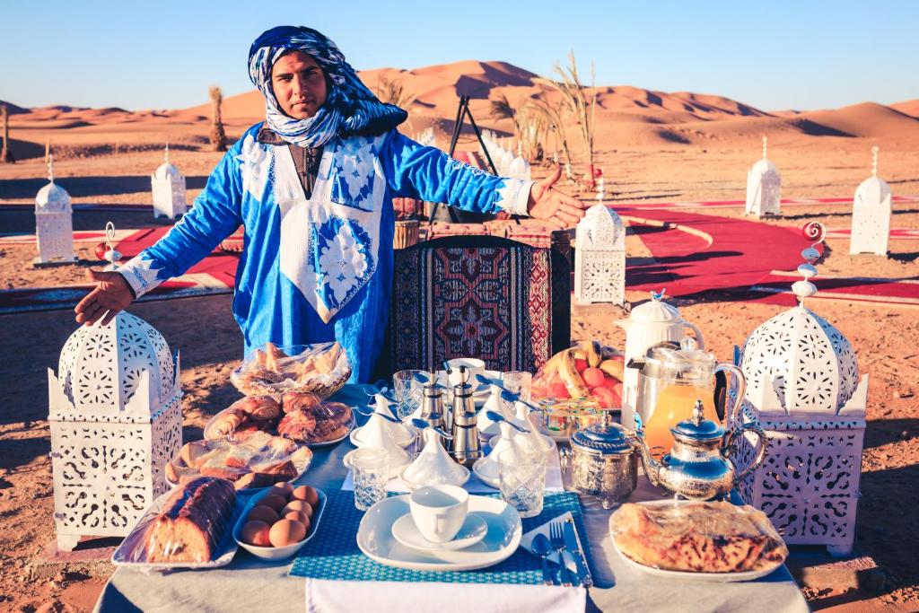 a man standing in front of a table with food at Luxury Desert Camp Amanar in Merzouga