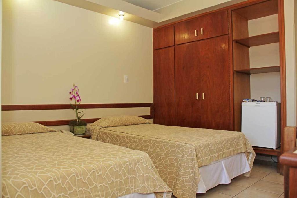 a bedroom with two beds and a refrigerator at Hotel Veredas in Paracatu