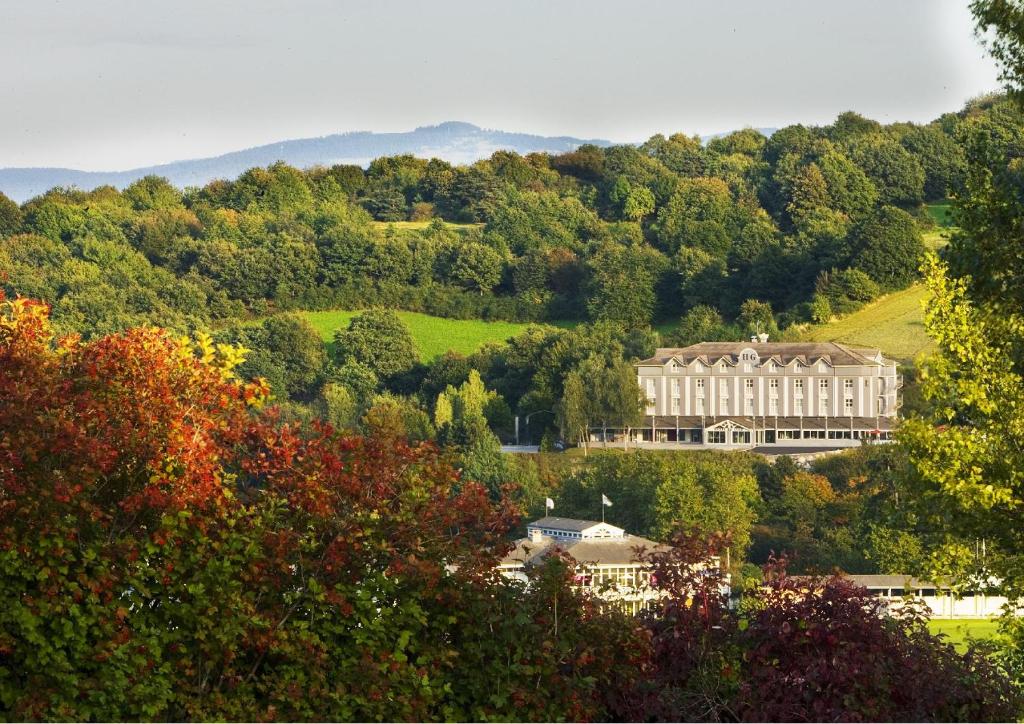 un grand bâtiment au sommet d'une colline plantée d'arbres dans l'établissement Hotel Du Golf, à Saint-Étienne