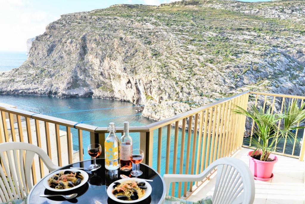 a table with food on a balcony with a view of the ocean at Avalon - Bellevue Gozo in Xlendi