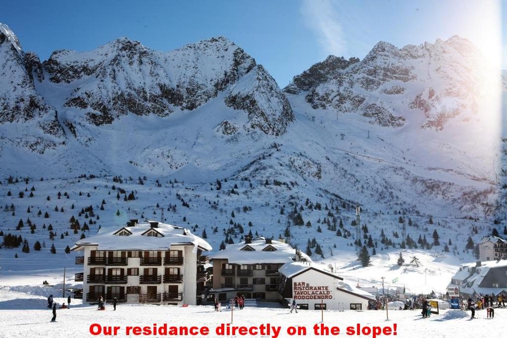 un edificio en la nieve con montañas en el fondo en Ski&Bike Apartment Passo Tonale en Ponte di Legno