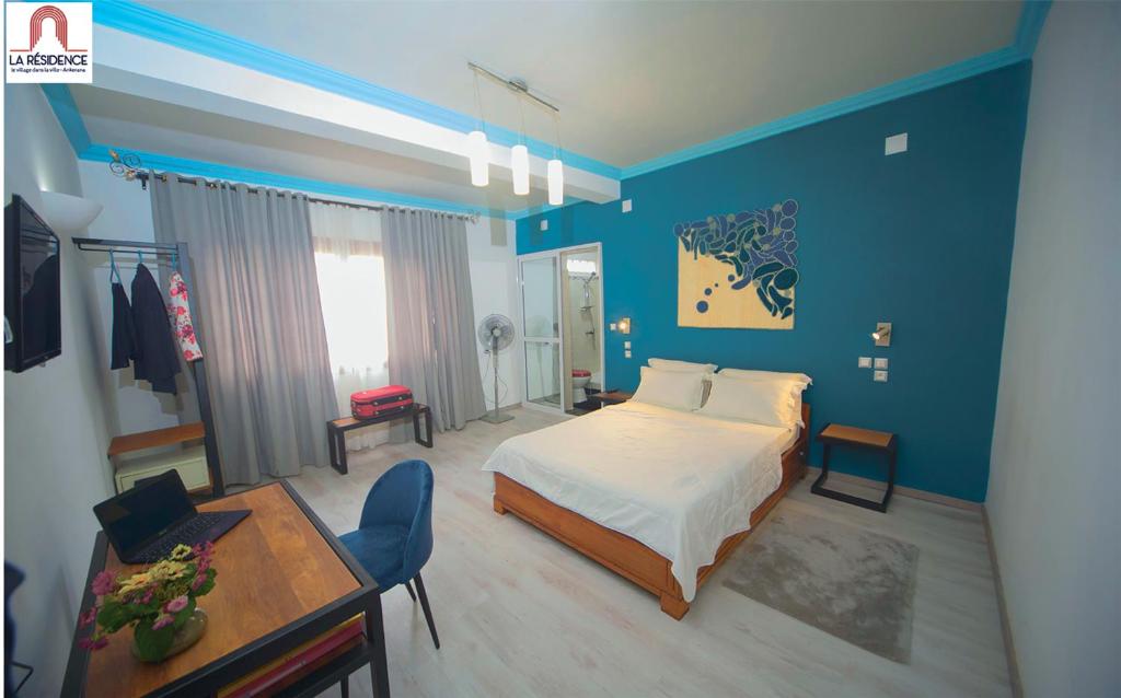 アンタナナリボにあるLa Résidence d'Ankeranaの青い壁のベッドルーム1室、ベッド1台、テーブルが備わります。