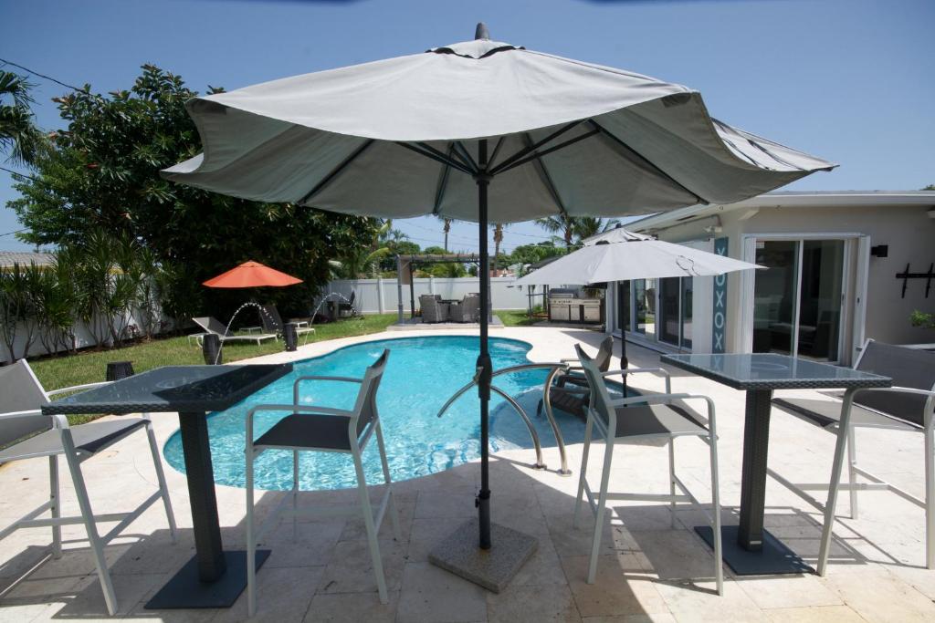 ein Regenschirm und zwei Tische und Stühle neben einem Pool in der Unterkunft Heated pool ,3 bedroom bungalow ,minutes from the beach in Deerfield Beach