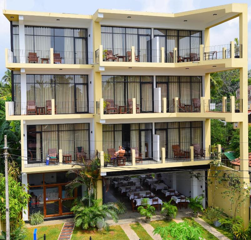 ein Apartmenthaus mit Balkonen, Tischen und Stühlen in der Unterkunft Chaaya inn Hotel in Hikkaduwa