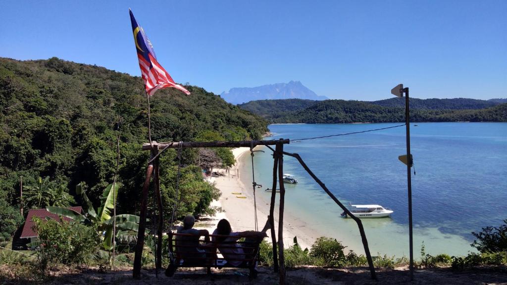 a couple sitting on a bench next to a beach at Bigfin beach resort in Kota Belud