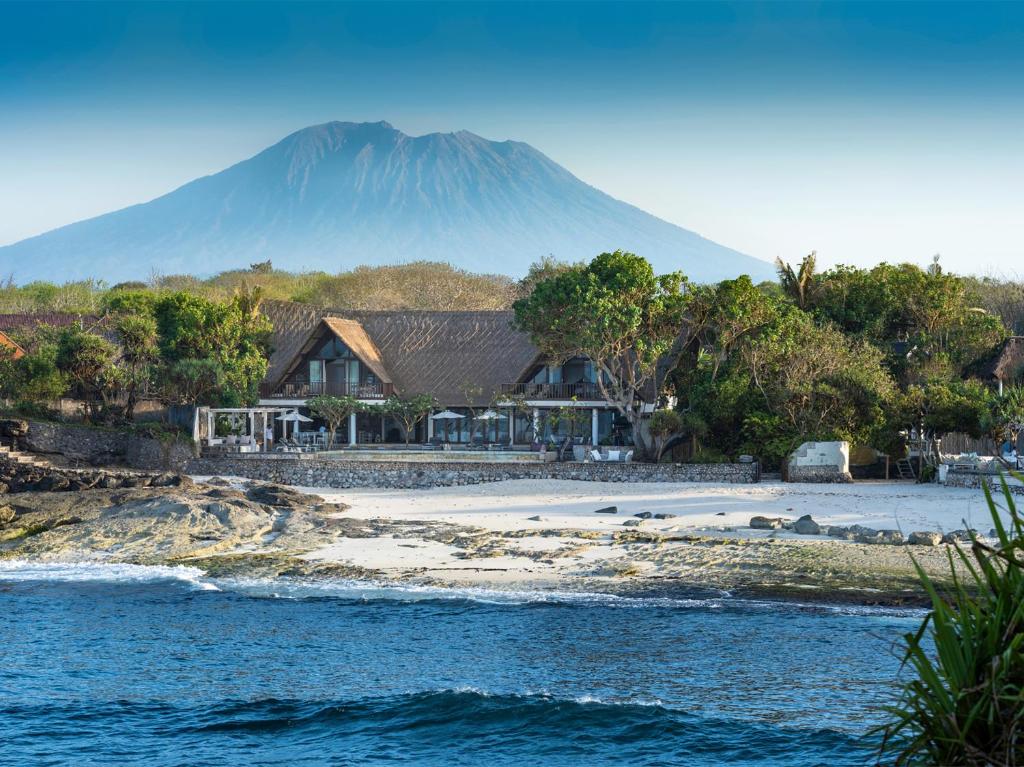 a house on a beach with a mountain in the background at Villa Voyage in Nusa Lembongan