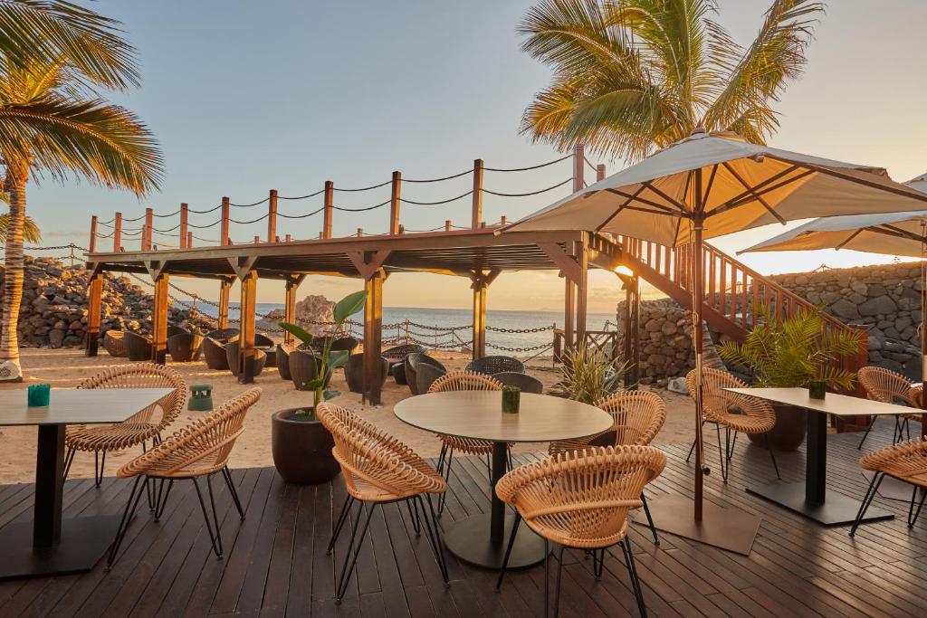 a patio with tables and chairs and the beach at Secrets Lanzarote Resort & Spa - Adults Only (+18) in Puerto Calero