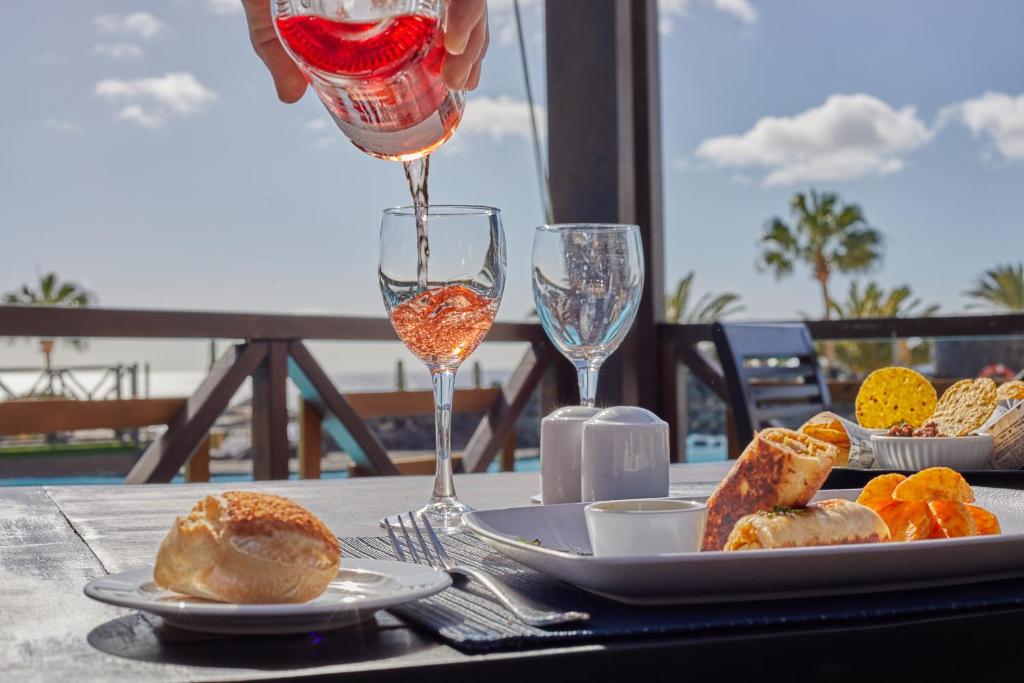 a person pouring a glass of wine on a table with food at Secrets Lanzarote Resort & Spa - Adults Only (+18) in Puerto Calero