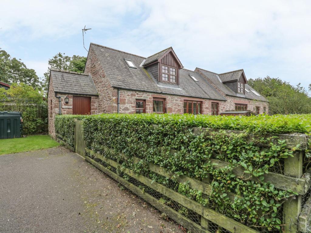 a stone house with a hedge in front of it at Kamba Cottage in Tannadice