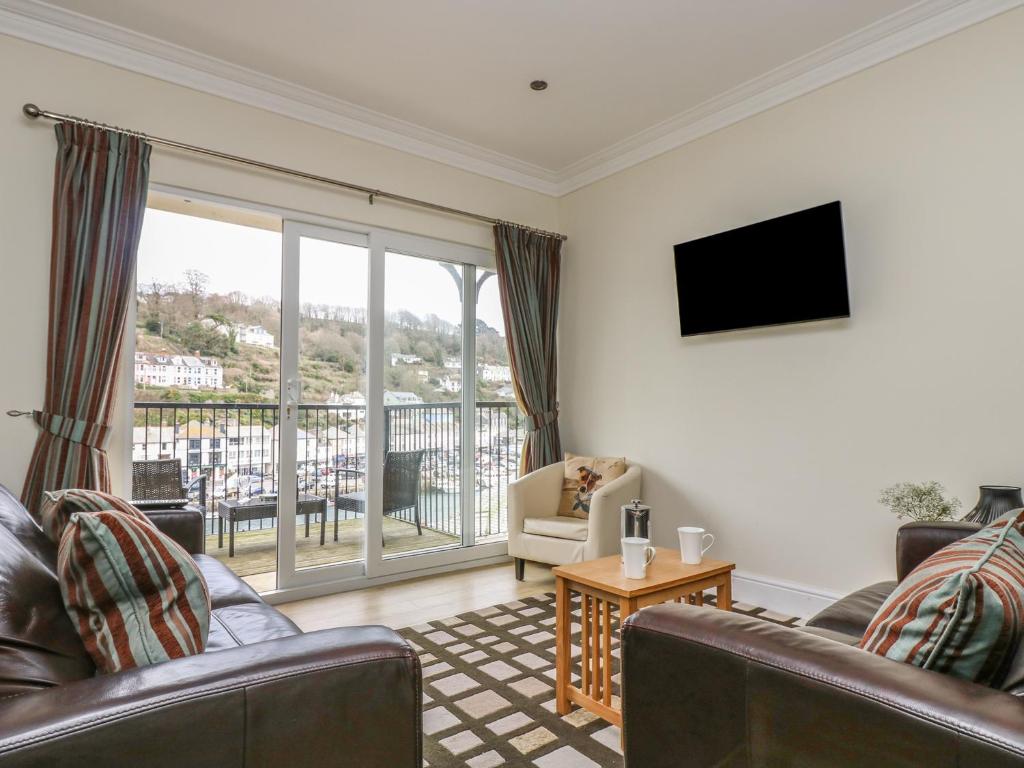 a living room with couches and a television and a balcony at Rivercrest in Looe