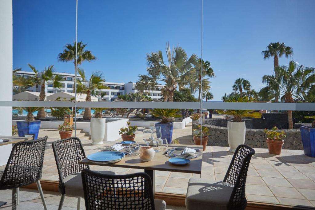 a table and chairs on a patio with palm trees at Secrets Lanzarote Resort & Spa - Adults Only (+18) in Puerto Calero