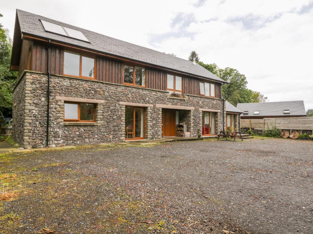 a stone house with a gravel driveway in front of it at Woodland Villa in Oban