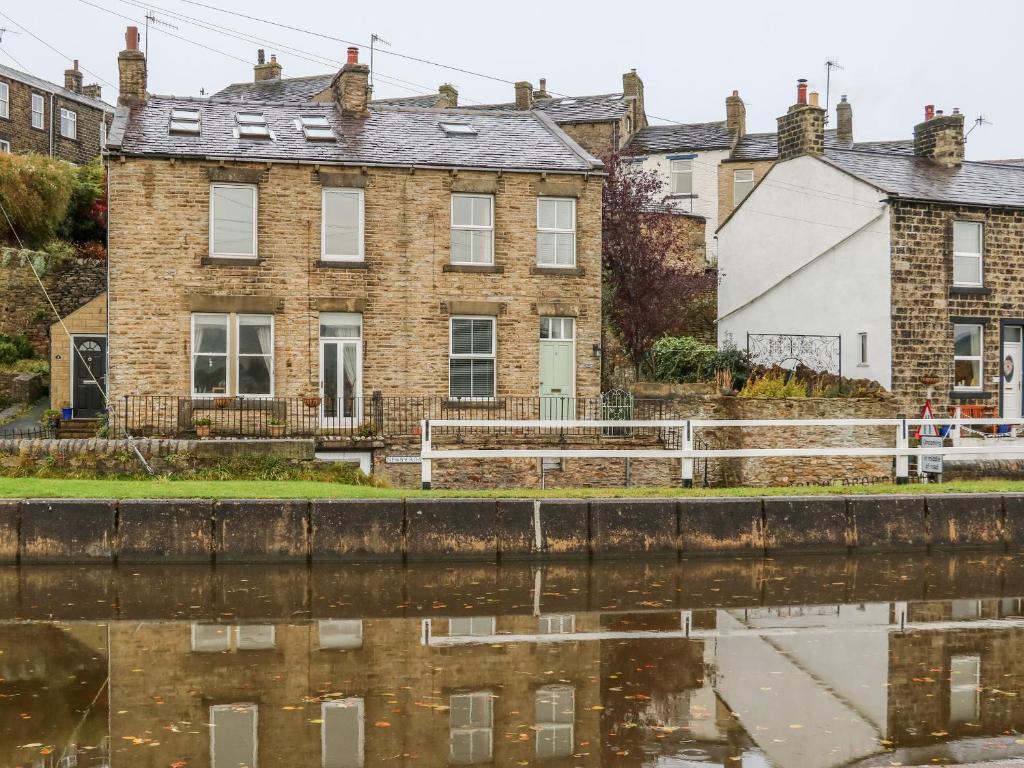 uma velha casa de tijolos ao lado de um corpo de água em Canalside Cottage em Kildwick