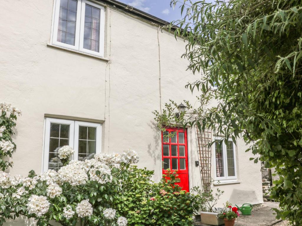 a white house with a red door and flowers at Tan Y Rhos Isa in Llansantffraid Glyn Ceiriog