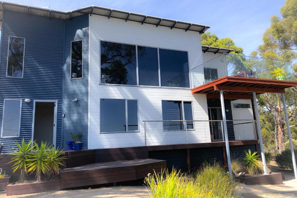 a blue and white house with a porch at BAY OF FIRES BEACH SHACK ocean views from a modern Beachhouse in Binalong Bay