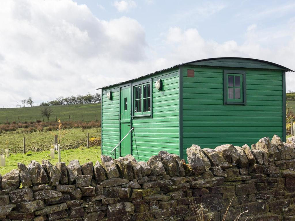 a green house behind a stone wall at Peat Gate Shepherd's Hut in Greenhead