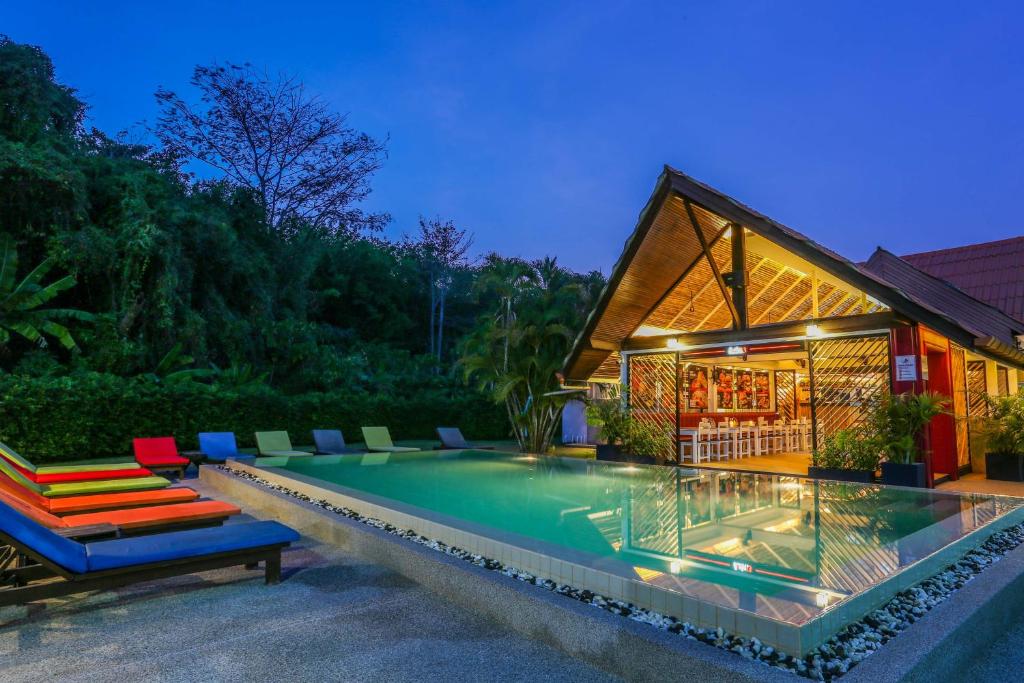 a swimming pool with chairs and a house at Naiharn Beach Resort - SHA Plus Extra in Nai Harn Beach