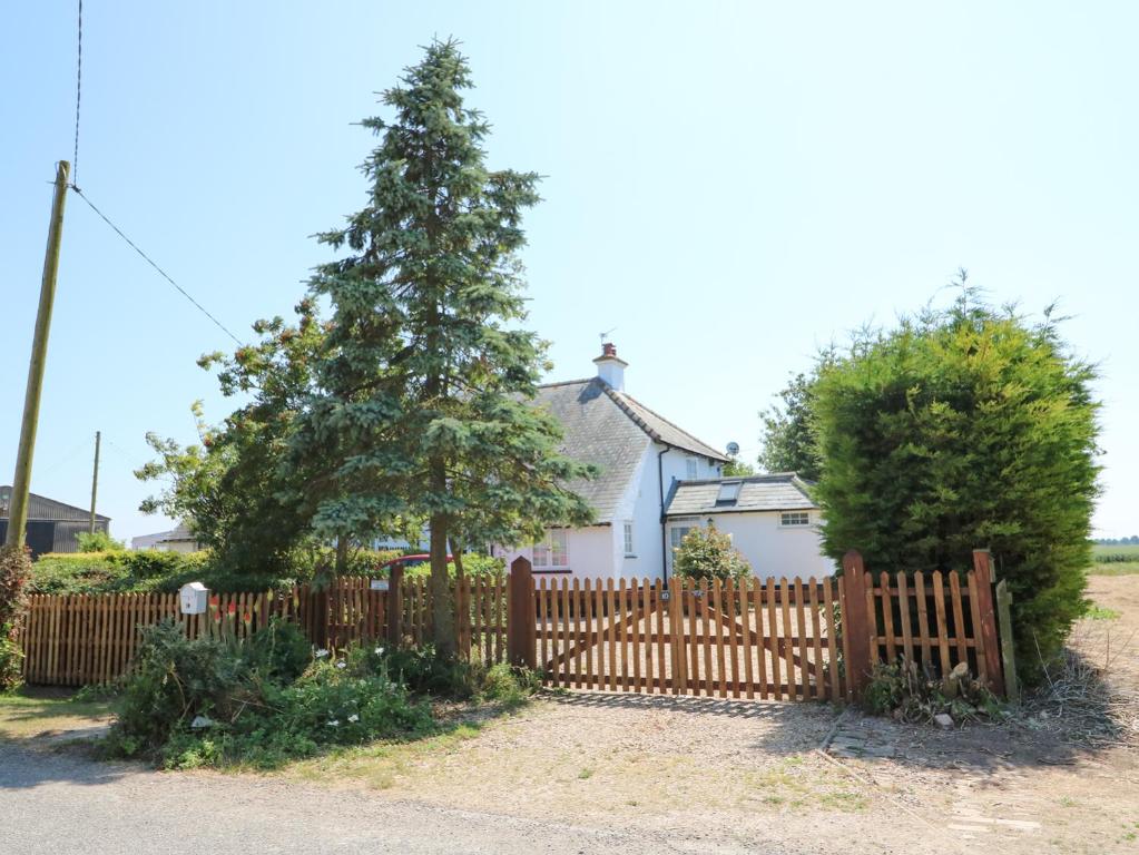 a wooden fence in front of a house with a tree at Grange Farm Cottage in Sutton Bridge