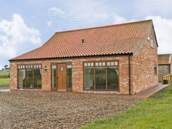 a brick house with glass doors on a field at Owl Cottage in Hedon