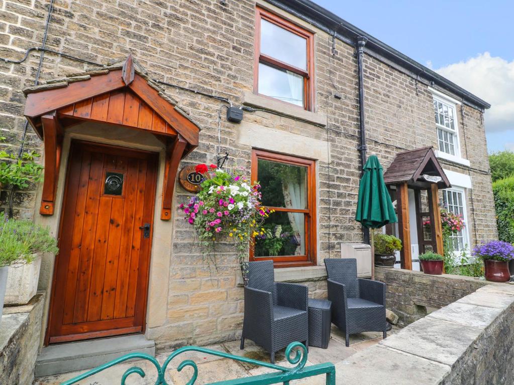 uma casa de tijolos com uma porta de madeira e cadeiras em Brook Cottage em Hayfield