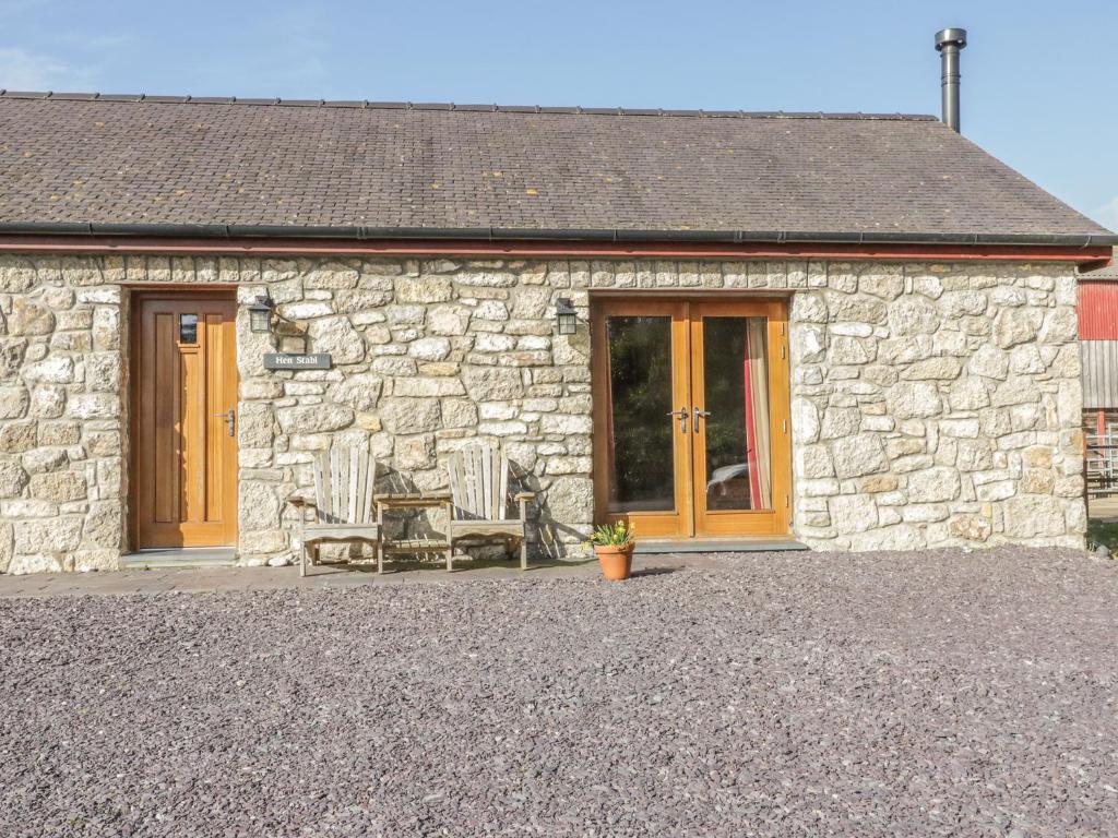 a stone cottage with two chairs and a door at Hen Stabl in Beaumaris