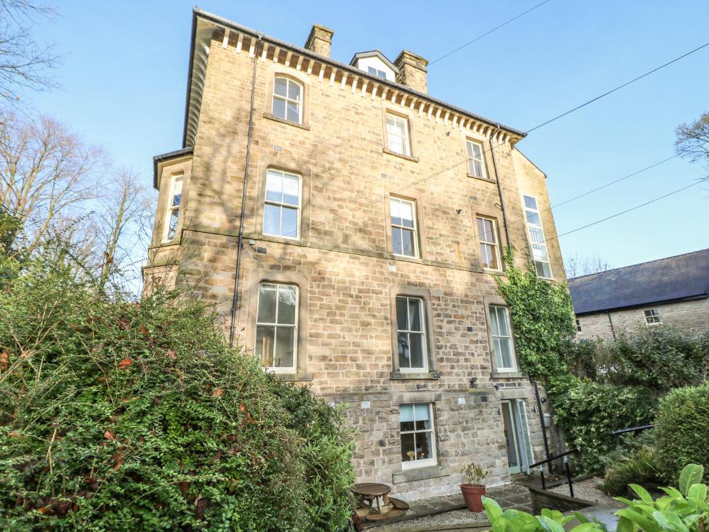 un antiguo edificio de ladrillo con ventanas y arbustos en The Garden Flat, en Buxton