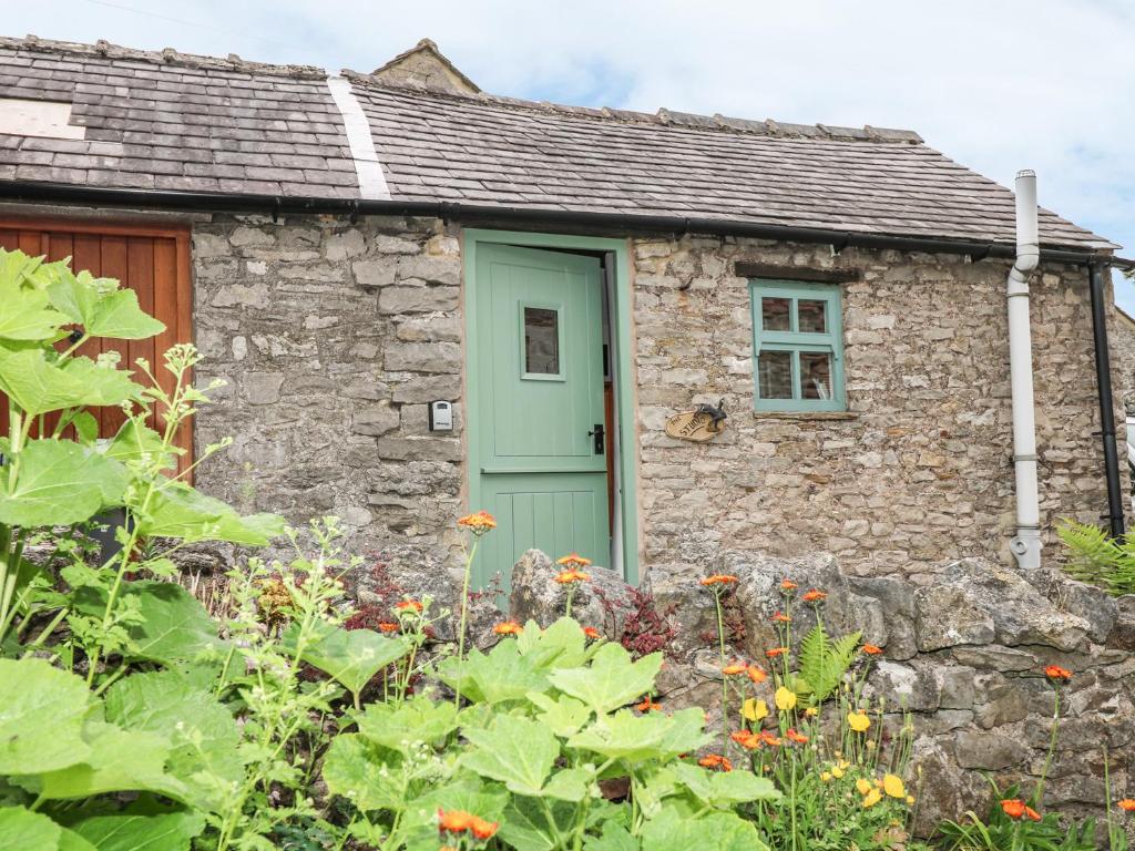 a stone cottage with a green door in a garden at The Studio in Bradwell