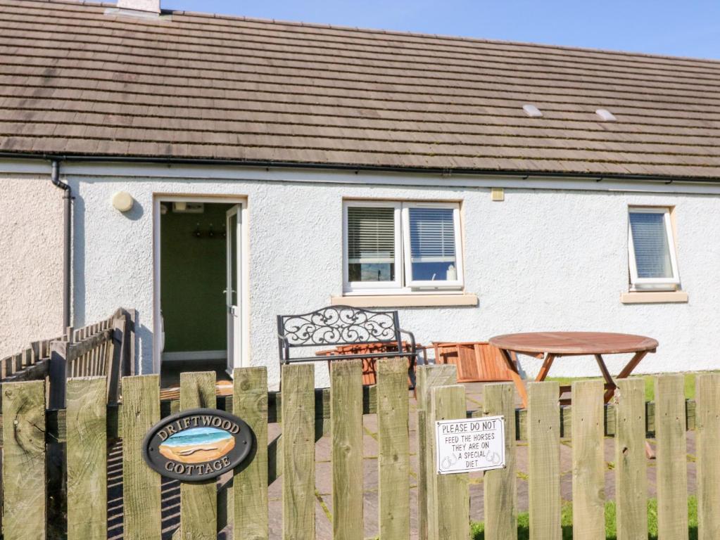 a white house with a wooden fence and a table at Driftwood Cottage in Craignure