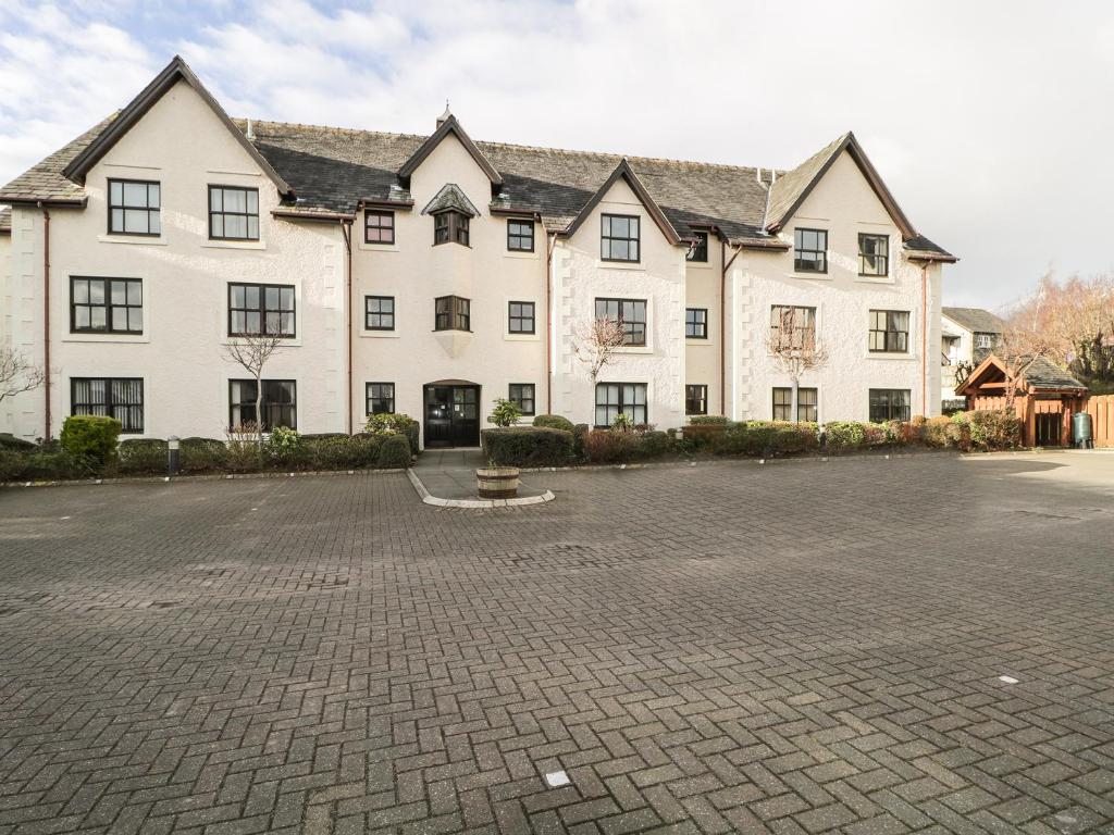 een groot wit gebouw met een bakstenen parkeerplaats bij Andra Ghyll in Keswick