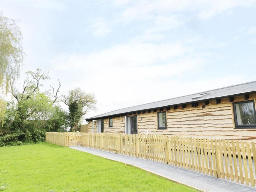 ein Holzhaus mit einem Zaun neben einem Hof in der Unterkunft Willow Lodge in Cleeve Prior