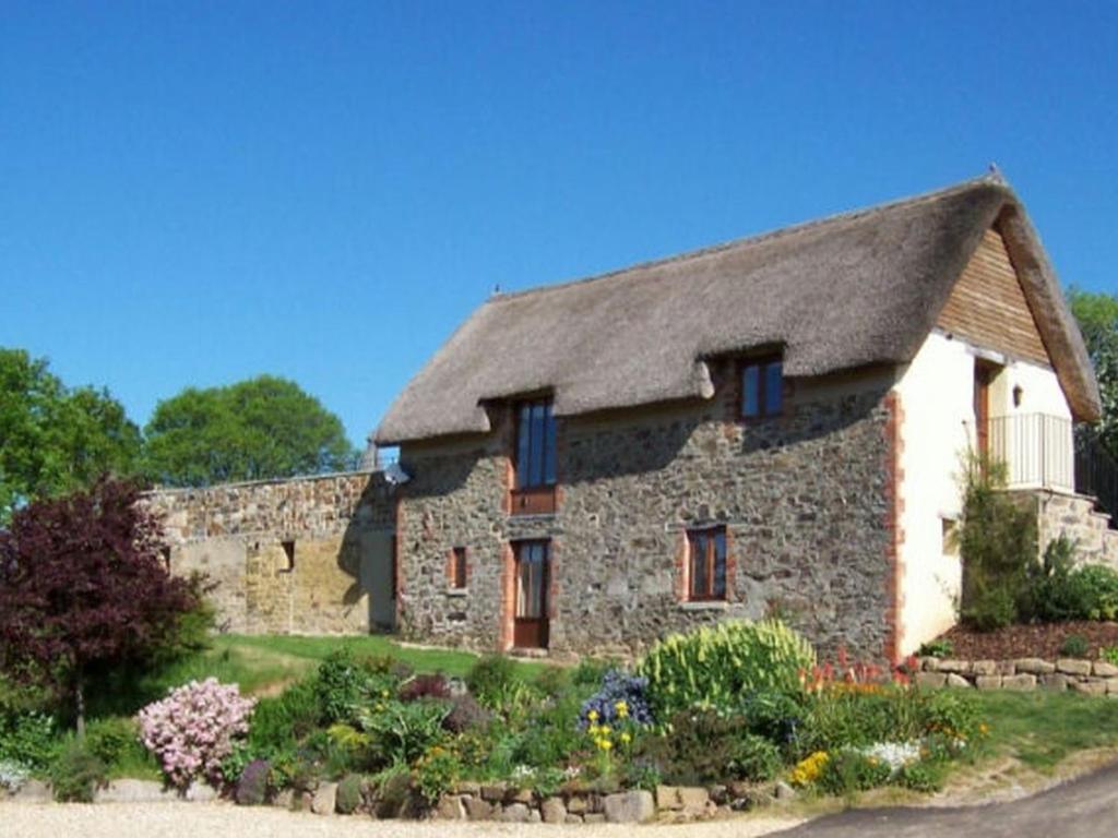 a stone house with a thatched roof and a garden at The Cottage in Sampford Courtenay