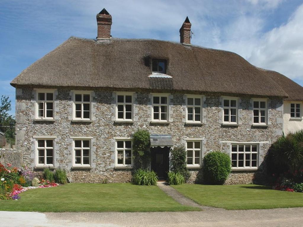 duży kamienny dom z dachem krytym strzechą w obiekcie Hornshayne Farmhouse w mieście Northleigh