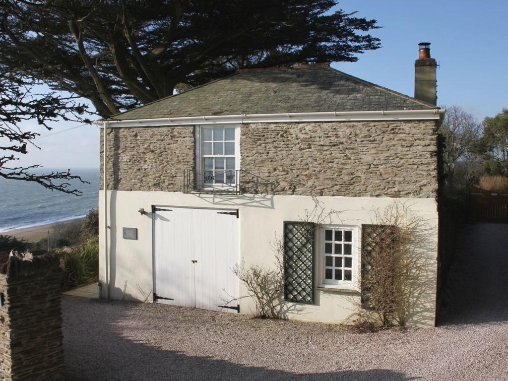 an old stone house with a white garage at Coach House Cottage in Strete