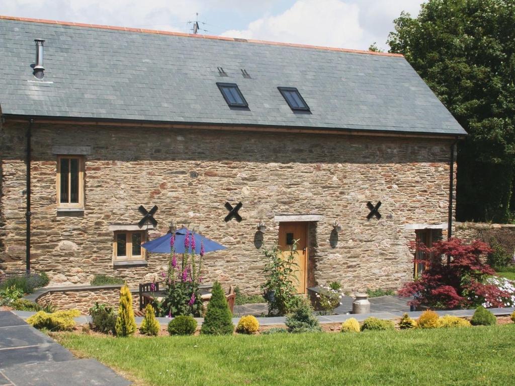 a stone house with an umbrella in front of it at The Hay Barn in Halwell