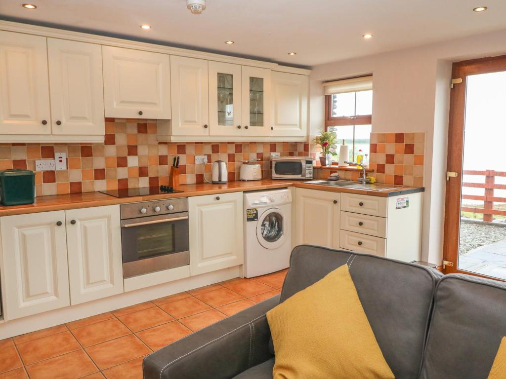 a kitchen with white cabinets and a couch at Cahirkeen Cottage in Eyeries