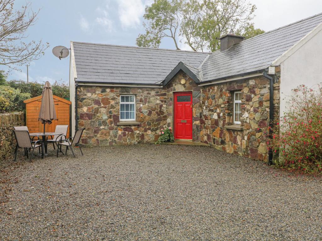 Ce cottage en pierre dispose d'une porte rouge, d'une table et de chaises. dans l'établissement Rose Cottage, à Ramsgrange