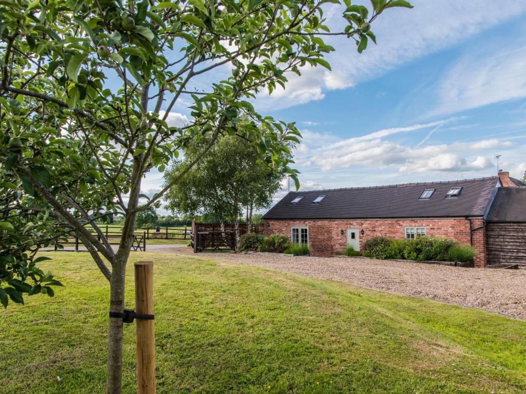 a brick barn with a tree in front of it at Barnfields Holiday Cottage in Kingsley
