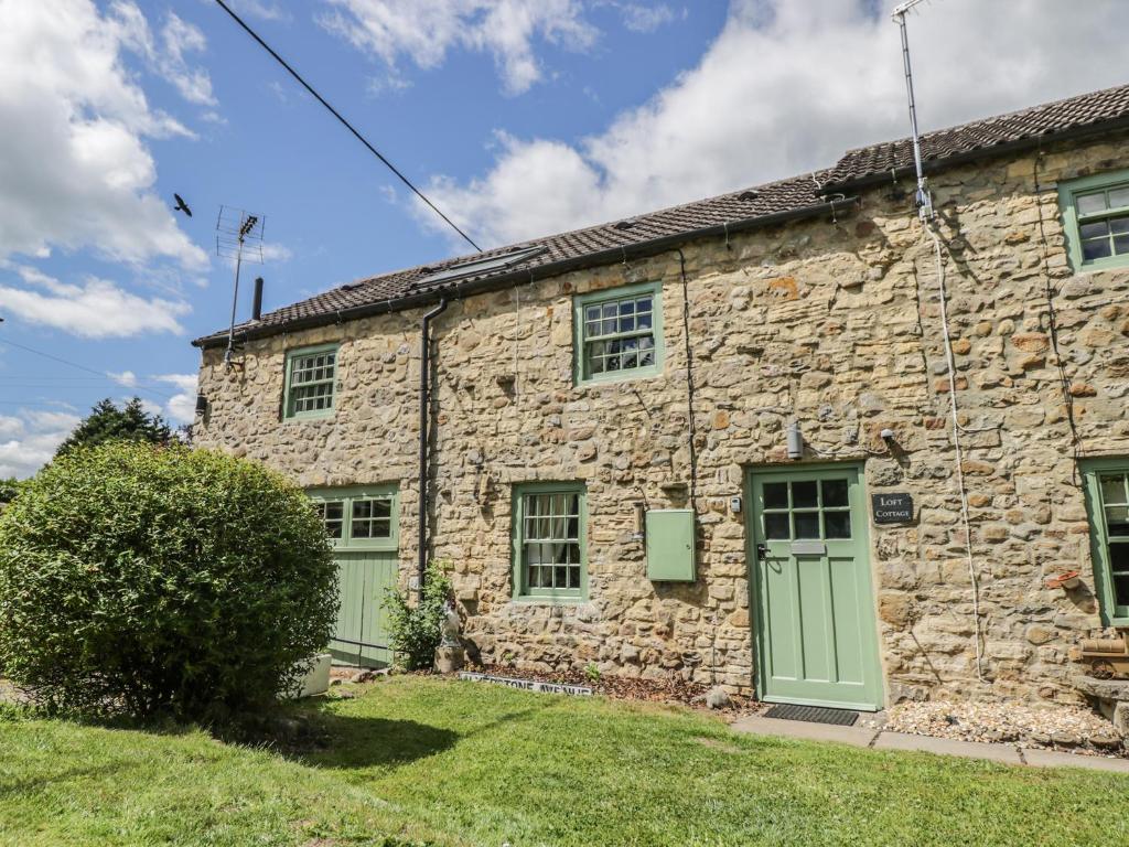 an old stone house with green doors and a yard at Loft Cottage in Bedale