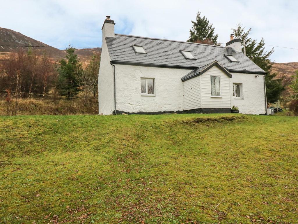 a white house on top of a grassy hill at Creag Mhor Cottage in Dornie