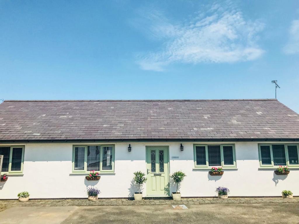 een wit huis met groene luiken en bloemen bij Orchard Cottage in Holywell