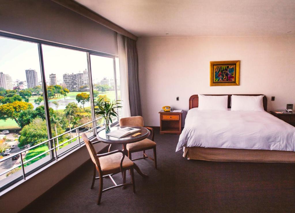 Cette chambre comprend un lit, une table et une grande fenêtre. dans l'établissement BTH Hotel Lima Golf, à Lima