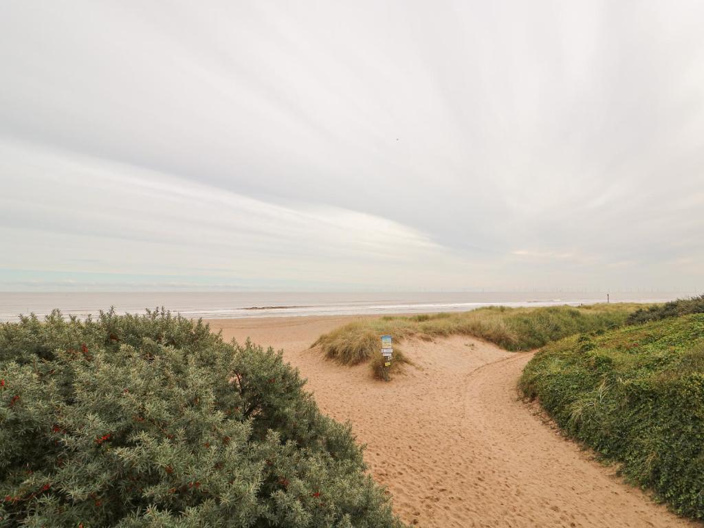 a dirt road leading to a beach with bushes at Moggs Retreat in Skegness