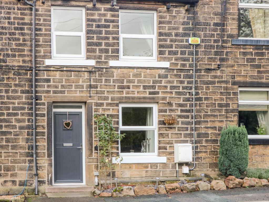 una casa de ladrillo con una puerta y ventanas negras en Springwood Cottage en Holmfirth