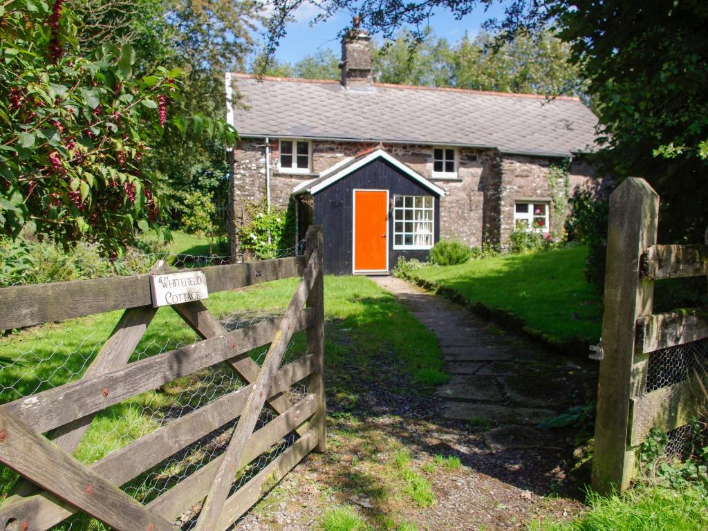 a farm house with an orange door and a fence at Whitefield Cottage in Barnstaple