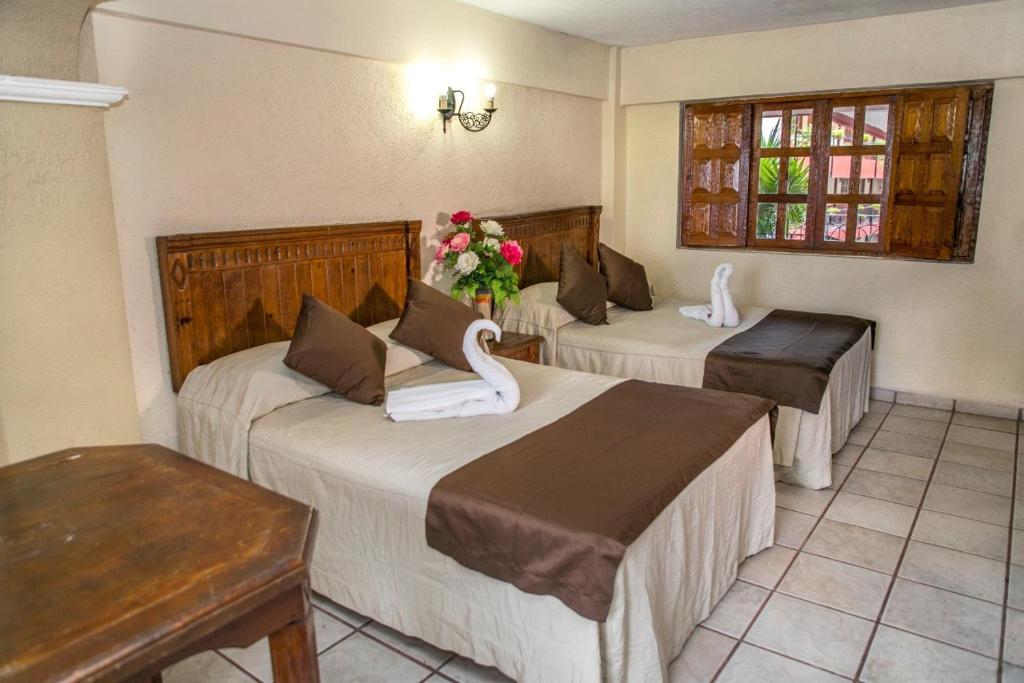 Hotel Hacienda María Eugenia في أكابولكو: غرفه فندقيه ثلاث اسره عليها بجعه
