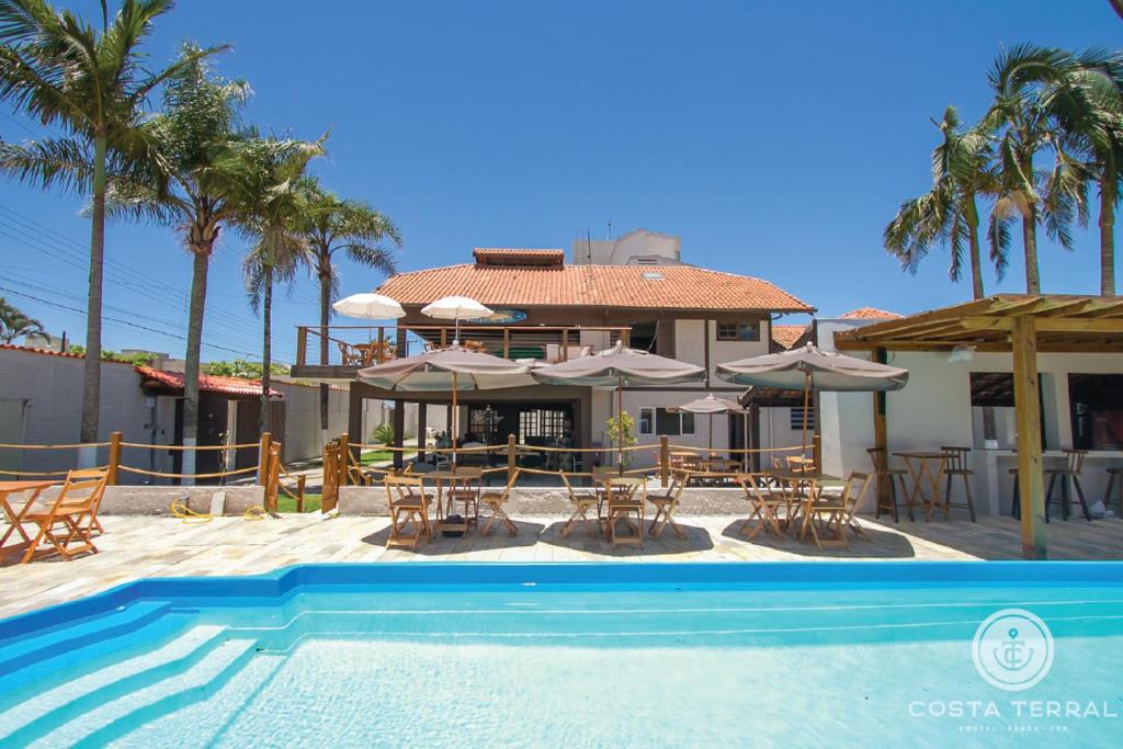 una casa con piscina con sillas y sombrillas en Costa Terral Hostel Beach Fun en Matinhos