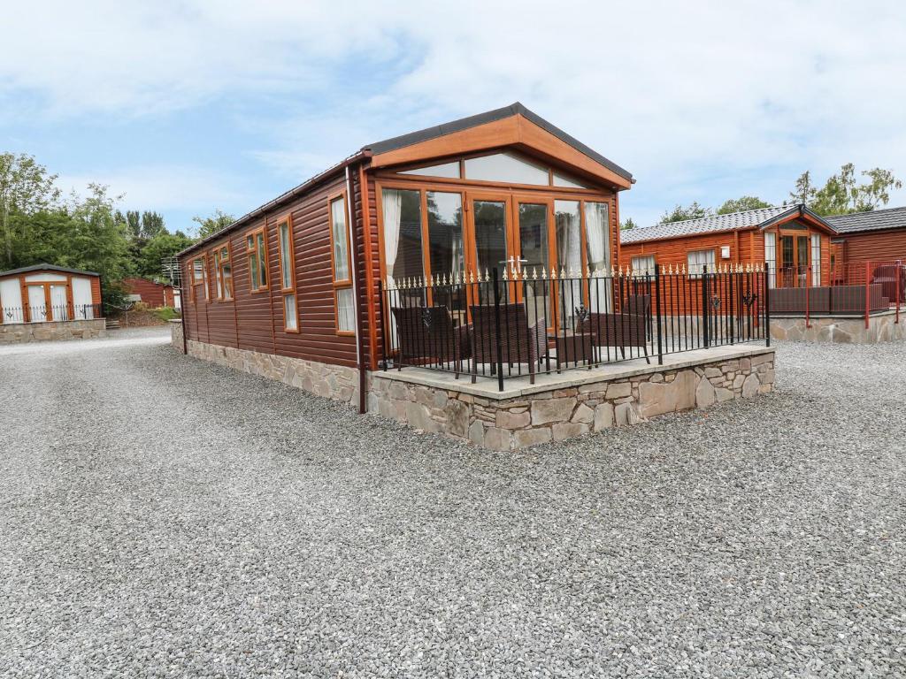 a small wooden cabin with a balcony on a gravel road at 32 Cruachan Lodge in Auchterarder