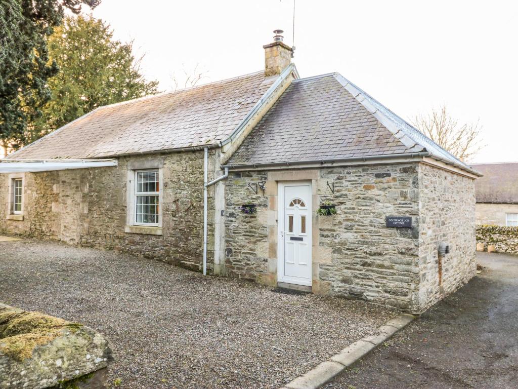 an old stone building with a white door at Colterscleuch Cottage in Hawick